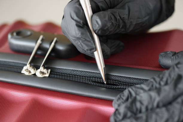 Thief in black gloves opening suitcase lock with ballpoint pen closeup